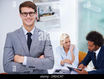 Er hat das Selbstvertrauen, zu führen. Porträt eines selbstbewussten Geschäftsmannes, der eine Brille mit Kollegen im Hintergrund trägt. Stockfoto