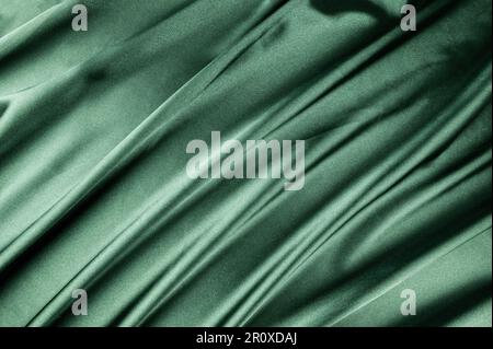 Luxuriöser grüner satinierter Hintergrund. Weiches und elegantes Seidenmaterial. Textil mit fließenden Wellen. Draufsicht, flach liegend. Stockfoto