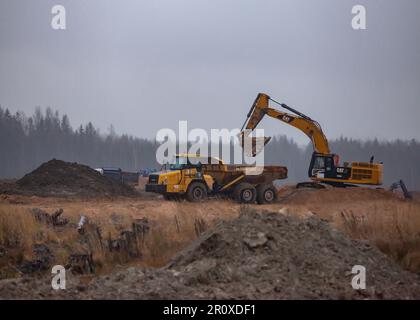 USt-Luga, Oblast Leningrad, Russland - 16. November 2021: Bagger Caterpillar belädt Kipper Komatsu. Fabrikbaustelle bei Regen Stockfoto