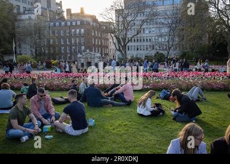 Touristen genießen die Krönungsblumen und den Abendsonnenschein in den Victoria Embankment Gardens im Zentrum von London, England, Großbritannien Stockfoto