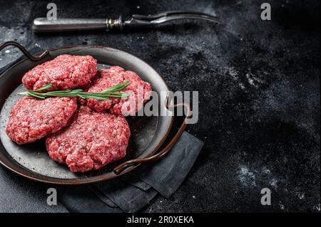 Ungekochte Frikadellen aus Hackfleisch, rohe Fleischschnitzel. Schwarzer Hintergrund. Draufsicht. Platz für Text. Stockfoto