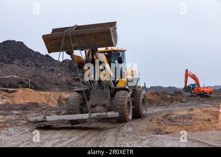 USt-Luga, Oblast Leningrad, Russland - 16. November 2021: Bulldozer transportiert Betonplatten zum Straßenbau Stockfoto