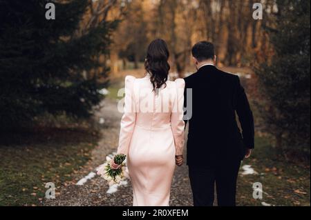 Ein gut gekleidetes Paar, das in einem grasbedeckten Außenbereich steht und Händchen hält Stockfoto