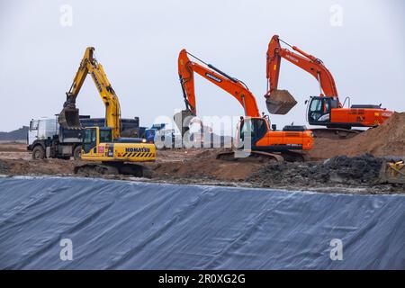 USt-Luga, Oblast Leningrad, Russland - 16. November 2021: Kunststoffabdeckung von Chemieabfallgräben. Bagger Hitachi, Comatsu, Doosan am Rand. Stockfoto