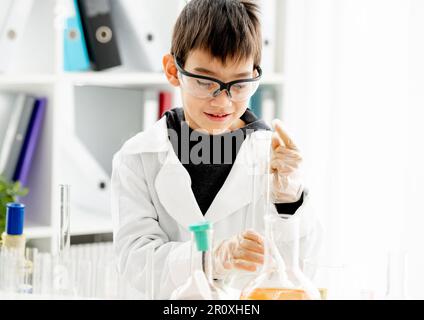 Schuljunge trägt Schutzbrille und macht Chemieexperiment in der Grundschule. Pupille mit Reagenzgläsern im Labor Stockfoto