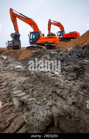 USt-Luga, Oblast Leningrad, Russland - 16. November 2021: Orangefarbene Bagger Doosan auf schmutzigem Boden Stockfoto