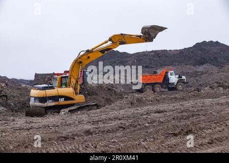 USt-Luga, Oblast Leningrad, Russland - 16. November 2021: Baustelle bei Regen. Bagger und Kipplaster bewegen sich auf dem Boden. Stockfoto