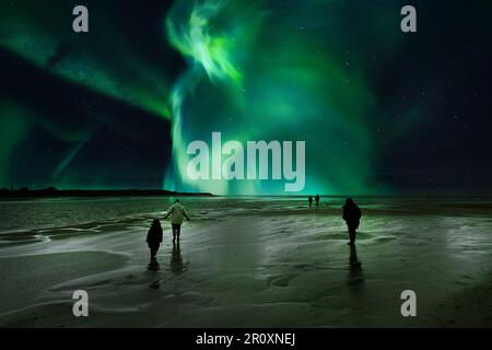 Die Menschen stehen am Strand und starren in Staunen auf die farbenfrohe Aurora Borealis am Nachthimmel Stockfoto