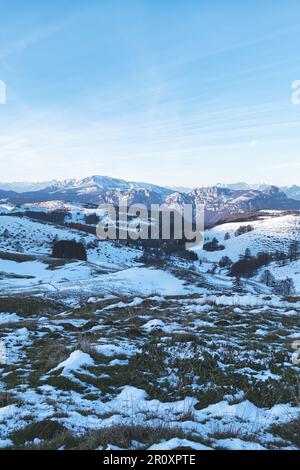 Eine atemberaubende Winterszene mit einer schneebedeckten Landschaft in der Nähe majestätischer Berge und grüner Felder Stockfoto