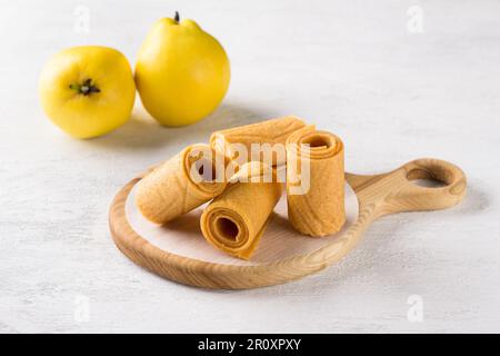 Natürliches Quittenpastille auf einem Holzbrett, umgeben von frischen Quittenfrüchten auf hellgrauem Hintergrund Stockfoto