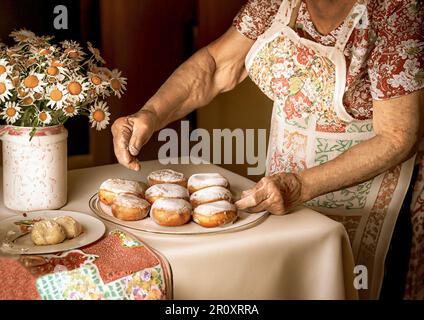 Eine alte Dame, die Donuts auf einem hölzernen Farmhaus-Tisch macht Stockfoto