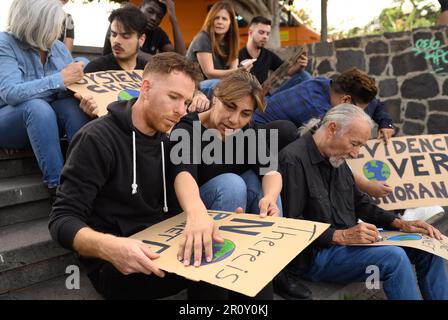 Eine Gruppe fokussierter, vielfältiger Demonstranten, die Kartonplakate kreieren, während sie während der Vorbereitung auf den Streik auf Treppen sitzen Stockfoto