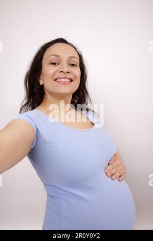 Nahaufnahme eines Selfie einer schönen schwangeren Frau, die Selfie macht und mit ausgestreckter Hand auf die Kamera ihres Smartphones schaut Stockfoto