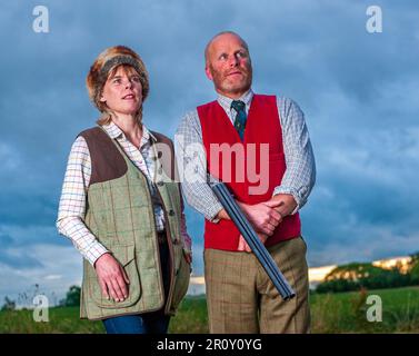 Eine englische Dame und ein Gentleman standen in der Dämmerung in Schießanzügen mit einer Schrotflinte Stockfoto