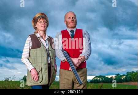 Eine englische Dame und ein Gentleman standen in der Dämmerung in Schießanzügen mit einer Schrotflinte Stockfoto