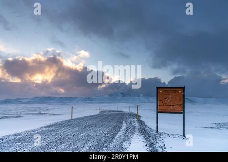 Panoramablick über eine Schneelandschaft in Island mit unbefestigter Schotterstraße und Warnschild auf Isländisch (englische Übersetzung auf dem Schild) Stockfoto