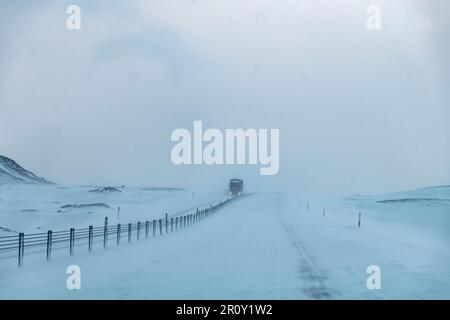 Sicht des Fahrers auf die Hauptstraße auf Island während eines Schneesturms mit schneebedeckter Straße und schlechter Sicht bei einem großen entgegenkommenden Lkw Stockfoto