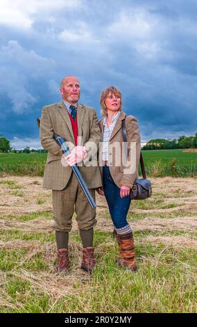 Eine englische Dame und ein Gentleman standen in der Dämmerung in Schießanzügen mit einer Schrotflinte Stockfoto