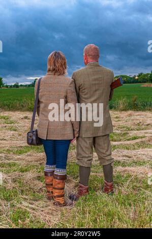 Eine englische Dame und ein Gentleman standen in der Dämmerung in Schießanzügen mit einer Schrotflinte Stockfoto