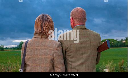 Eine englische Dame und ein Gentleman standen in der Dämmerung in Schießanzügen mit einer Schrotflinte Stockfoto