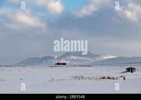 Panoramablick über schneebedeckte Landschaft mit schneebedeckten Bergen im schimmernden Wintersonnenlicht im Hintergrund auf Island mit einem hellroten Truck Stockfoto
