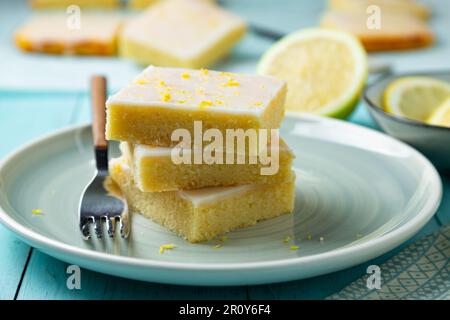 Zarte Zitronenbrownies mit Zitronenglasur und Schale auf einem Aquamaringericht Stockfoto