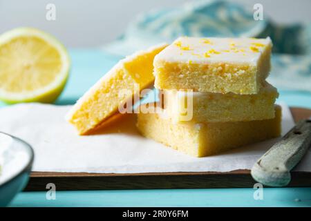 Zarte Zitronenbrownies mit Zitronenglasur und Schale auf Backpapier auf aquamarinem Hintergrund Stockfoto