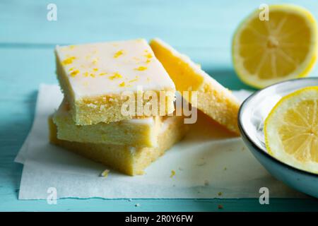 Zarte Zitronenbrownies mit Zitronenglasur und Schale auf Backpapier auf aquamarinem Hintergrund Stockfoto