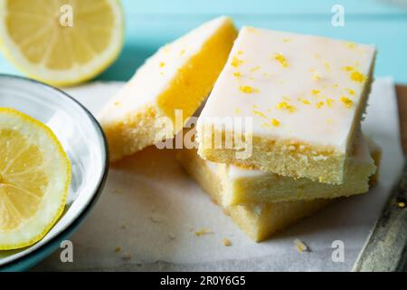 Zarte Zitronenbrownies mit Zitronenglasur und Schale auf Backpapier auf aquamarinem Hintergrund Stockfoto