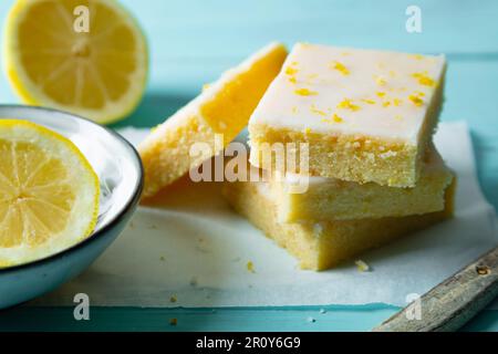 Zarte Zitronenbrownies mit Zitronenglasur und Schale auf Backpapier auf aquamarinem Hintergrund Stockfoto