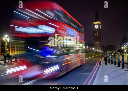 LONDON - 21. April 2023: Der ikonische rote Doppeldeckerbus ist ein Symbol für Londons Nachtrausch, der hier in einem Langzeitfoto auf Westminster Brian festgehalten wurde Stockfoto