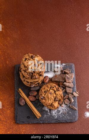 Ein kleiner Haufen Kekse mit Schokoladenstückchen. Studiofoto im rustikalen Hintergrund mit warmer Atmosphäre im Retro-Stil. Stockfoto
