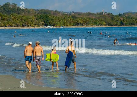 Strandliebhaber genießen diese beliebte palmengesäumte weiße Sandbucht in dieser entspannten Küstenstadt & Resort. Samara, Halbinsel Nicoya, Guanacaste, Costa Rica. Stockfoto