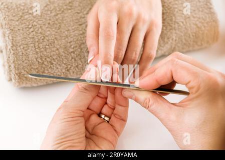 Von oben, von einem nicht erkennbaren männlichen Meister, der Nagelfeile benutzt, während er Maniküre an eine Kundin im leichten Schönheitssalon macht Stockfoto