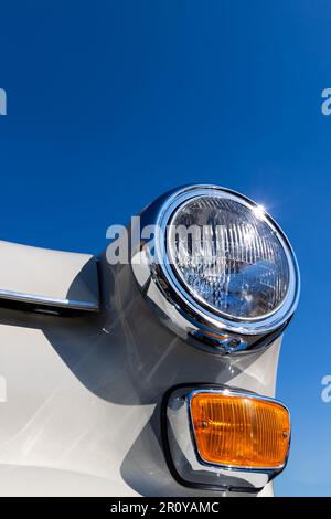 Nahaufnahme der runden Scheinwerfer und des orangefarbenen Blinkers eines weißen Oldtimers. Wunderschön restaurierte Chromdetails eines historischen Fahrzeugs. Stockfoto