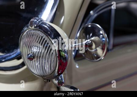 Nahaufnahme der runden Scheinwerfer eines beigen Oldtimers. Wunderschön restaurierte Chromdetails eines historischen Fahrzeugs. Stockfoto