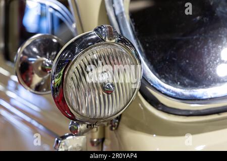 Nahaufnahme der runden Scheinwerfer eines beigen Oldtimers. Wunderschön restaurierte Chromdetails eines historischen Fahrzeugs. Stockfoto