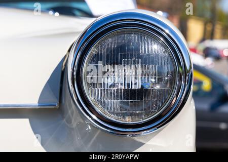 Nahaufnahme der runden Scheinwerfer eines weißen Oldtimers. Wunderschön restaurierte Chromdetails eines historischen Fahrzeugs. Stockfoto