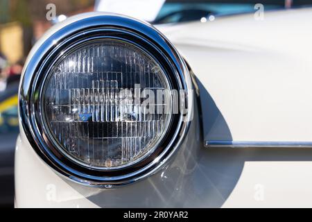 Nahaufnahme der runden Scheinwerfer eines weißen Oldtimers. Wunderschön restaurierte Chromdetails eines historischen Fahrzeugs. Stockfoto