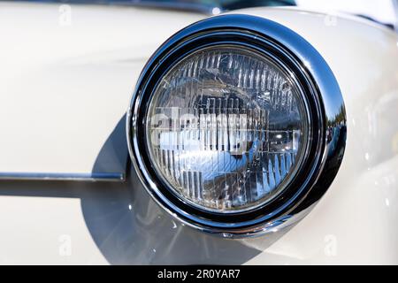 Nahaufnahme der runden Scheinwerfer eines weißen Oldtimers. Wunderschön restaurierte Chromdetails eines historischen Fahrzeugs. Stockfoto