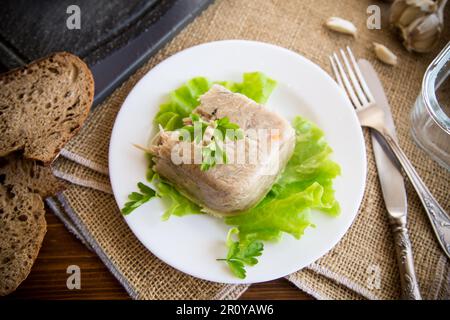 Gekochtes Hühnerfleisch in Fleischgelatinebrühe auf einem Teller auf einem Holztisch Stockfoto