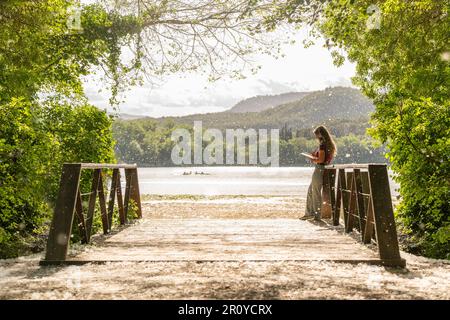 Landschaft mit einer Brücke und einem See im Hintergrund und einer jungen Frau, die schreibt Stockfoto