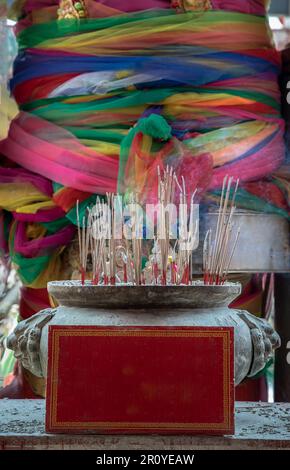 Weihrauch brennt in einem Incense Brenner Vorderseite von Fabrics bunt um den Big Tree gewickelt. Das mehrfarbige Tuch, das um einen Baum gebunden ist, ist der Glaube Stockfoto