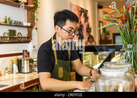 Vietnamesischer Kellner, der an der Theke arbeitet, mit einem Automaten in einem Café Stockfoto