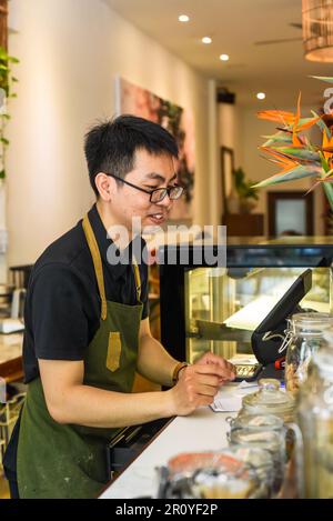 Vietnamesischer Kellner, der an der Theke arbeitet, mit einem Automaten in einem Café Stockfoto