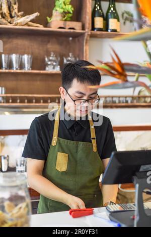 Vietnamesischer Kellner, der an der Theke arbeitet, mit einem Automaten in einem Café Stockfoto