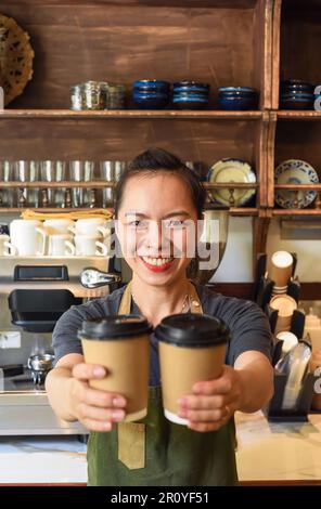 Vietnamesische lächelnde Kellnerin hielt Pappbecher mit Kaffee in einem Café Stockfoto