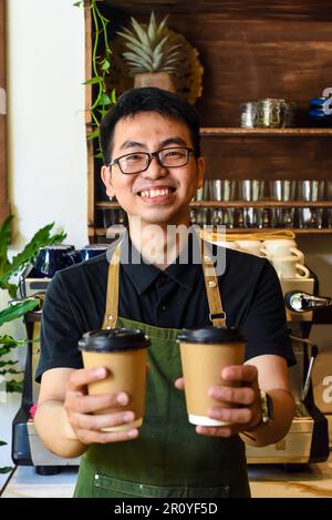 Vietnamesischer lächelnder Kellner hielt Pappbecher mit Kaffee in einem Café Stockfoto