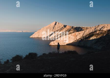 Panoramablick auf die Klippen der griechischen Insel folegandros, erleuchtet in warmen Farben des Sonnenuntergangs mit der Silhouette eines Mannes Stockfoto