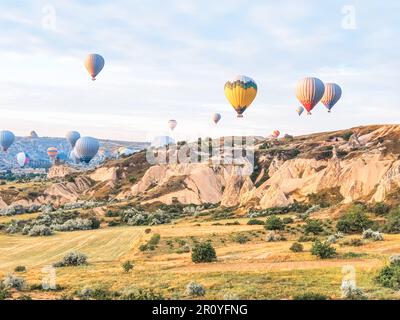 Fliegen Sie im Himmel viele bunte, wunderschöne Ballons in die Luft in Kappadokien in den Bergen früh bei Sonnenaufgang und Dämmerung. Füllung des Ballons mit Heißluft aus Bur Stockfoto